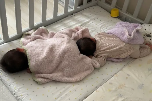 2人の赤ちゃんがベビーベッドで縦に並んで寝ている写真